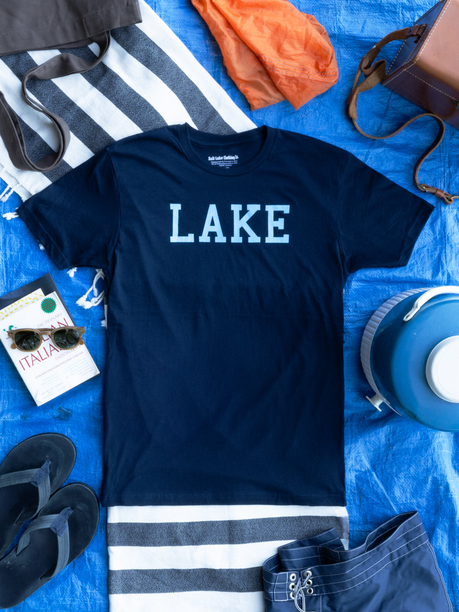 The Lake T - seen here with towels, sunscreen, sunglasses, and a book - everything you need for a perfect relaxing day by the water.